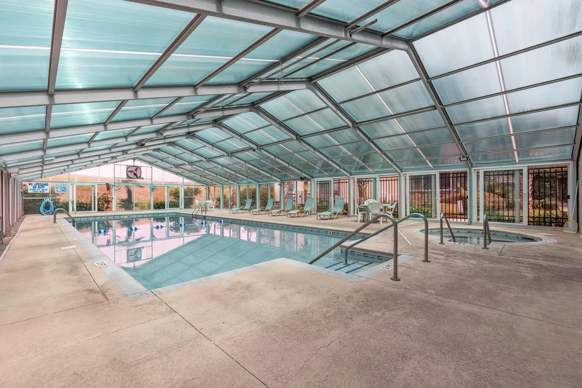 An indoor swimming pool with comfortable lounge chairs and expansive windows letting in natural light. The tranquil environment is ideal for all-weather swimming and quiet relaxation.