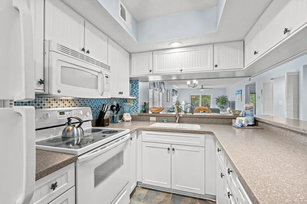 This image showcases a vibrant, well-lit kitchen with a spacious countertop, modern appliances, a colorful backsplash, and a window letting in natural light. The scene suggests a welcoming atmosphere perfect for cooking, socializing, and family gatherings.